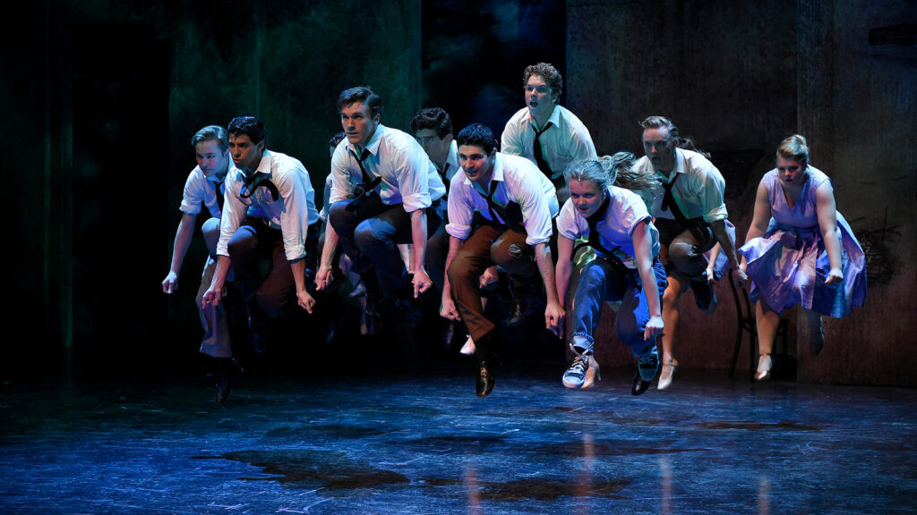 Dancers wearing white button down shirts and black ties jumping in unison