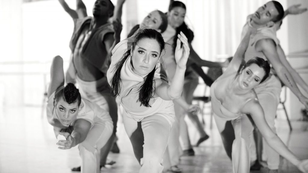 A group of dancers lunge toward the camera with their arms outstretched