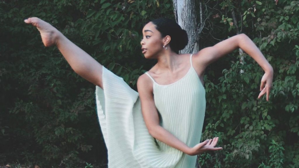 Londyn Alexander barefoot wearing a light green sleeveless dress dancing in front of bushes