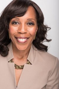 Woman wears a beige blazer and smiles at the camera