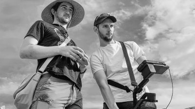 Black and white photo of Justin Epstein and Adam Agostino behind the scenes of a film shoot