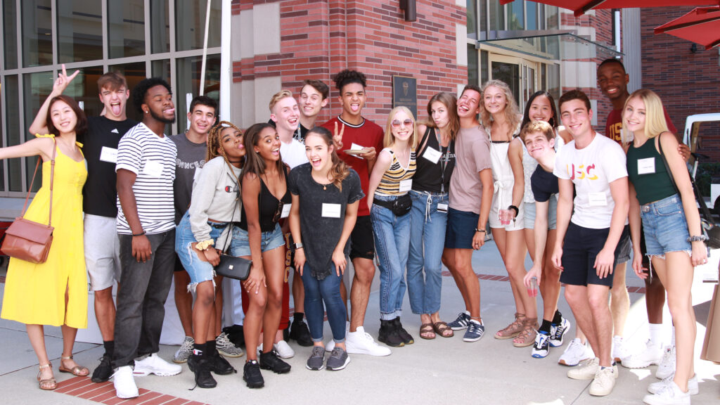 group of students pose and smile in front of brick building