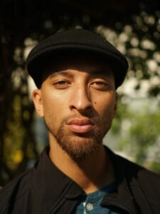 person in hat looking to camera with squinted eyes and a smirk for a headshot photo.