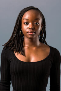 A woman with dark hair wearing a black shirt and gold earrings looks at the camera.