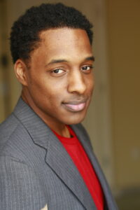 person photographed for headshot in grey tuxedo with red shirt underneath looking to the camera