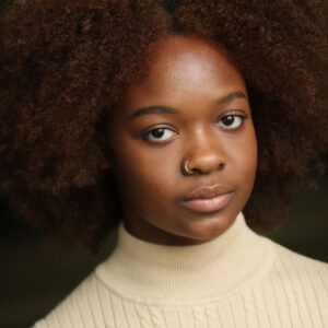 A person with a brown afro looking at the camera with a straight expression for headshot.