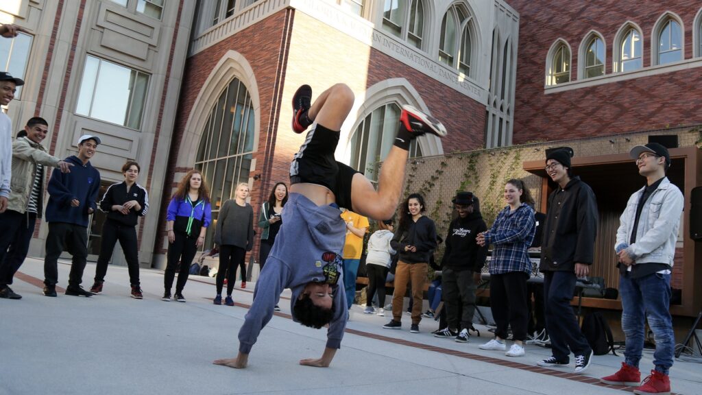 a group of people stand in a circle while a man handstands in the middle