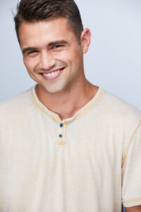 Casey Murray smiling and wearing a light yellow henley shirt