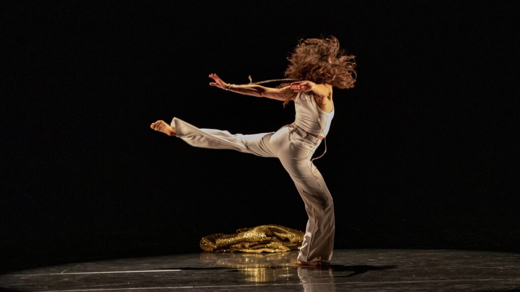 woman dressed in all white dancing alone onstage with her back leg extended