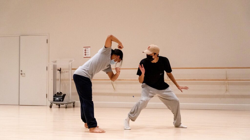 two dancers in a studio, wearing t-shirts and sweatpants