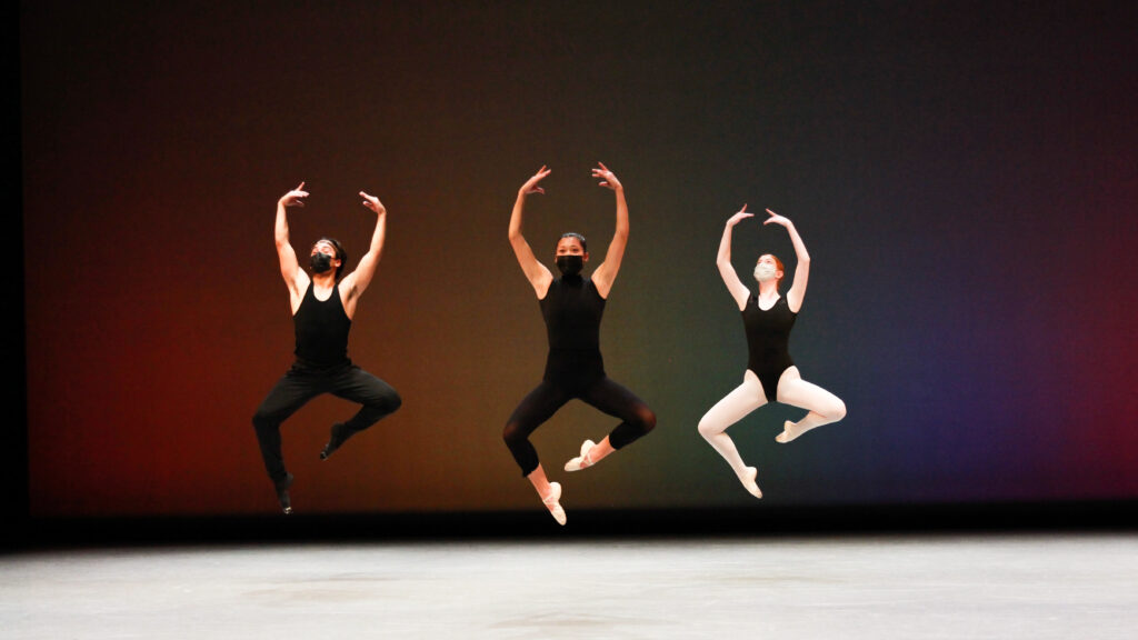 three dancers mid jump, wearing all black