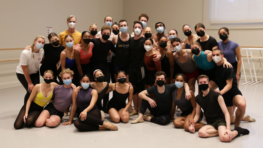 Students standing and sitting on the floor of a studio wearing masks and posing for a group photo