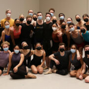 Students standing and sitting on the floor of a studio wearing masks and posing for a group photo