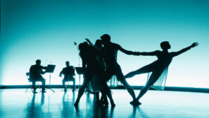 four dancers silhouetted in front of a group of musicians