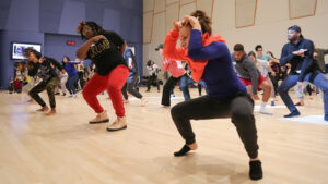 Students dancing in a studio with wood floors and a purple wall