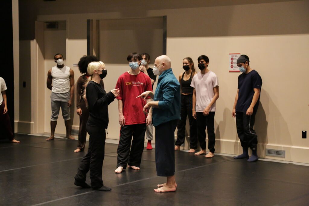 a group of students stand in a studio talking to choreographer Doug Varone