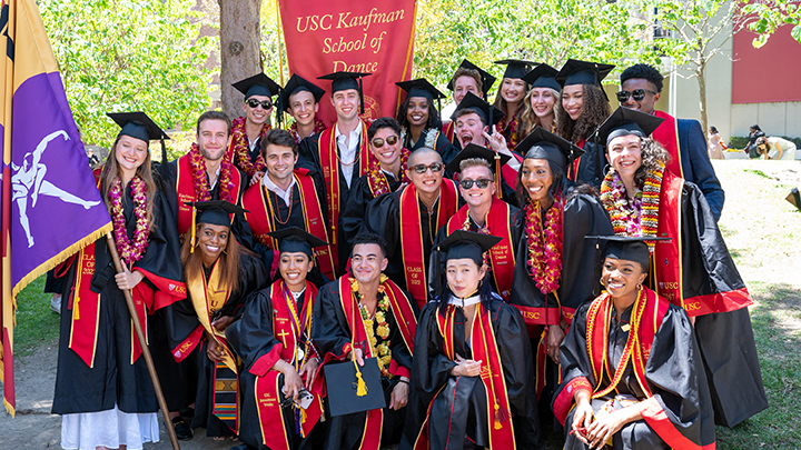 group of graduates smiling wearing black commencement robes and cardinal colored sashes