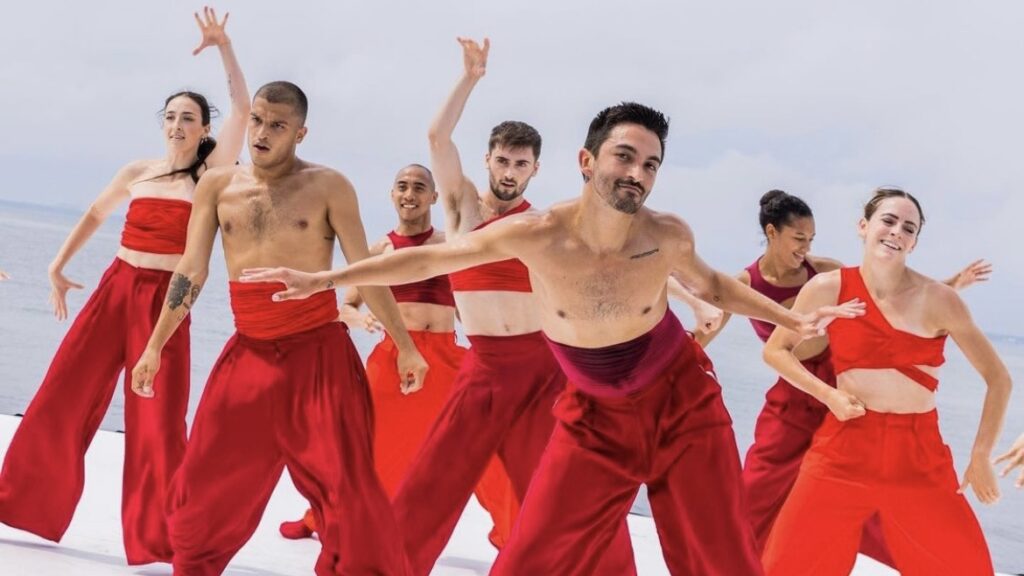 a group of dancers in red costumes dance on an outdoor stage