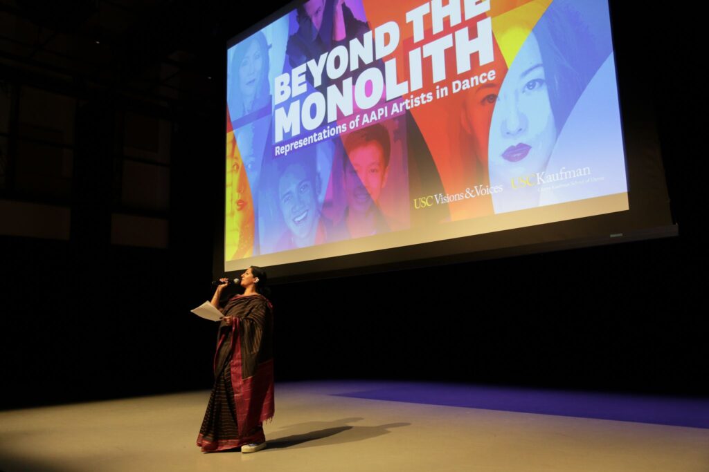 Achinta S. McDaniel stands in front of a project screen speaking into a microphone