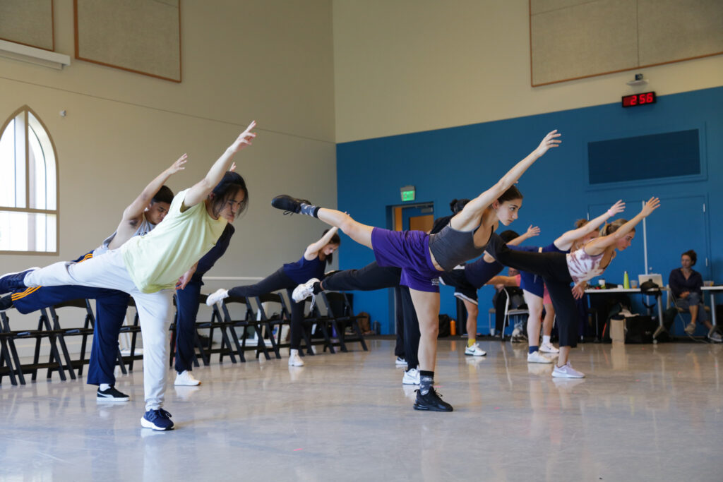 dancers in a studio. They all have one arm up and one leg in arabesque. 