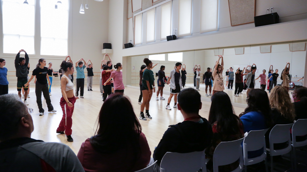 parents sit in a row of chairs watching students dancing in the studio