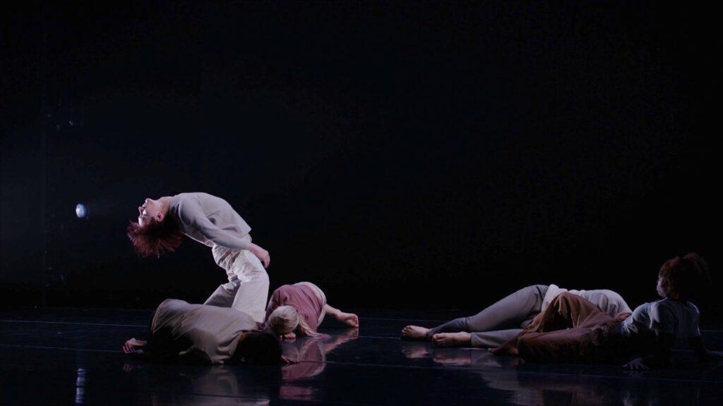 3 dancers lying on the floor, one in a backbend